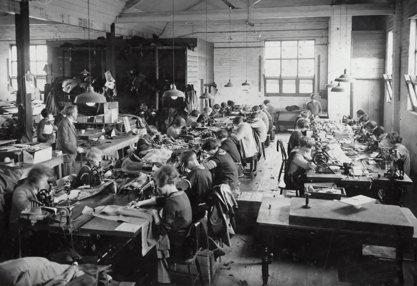 Table de coupe en atelier avec un rouleau de tissu déployé, patron papier posé et opérateur utilisant un cutter circulaire.
