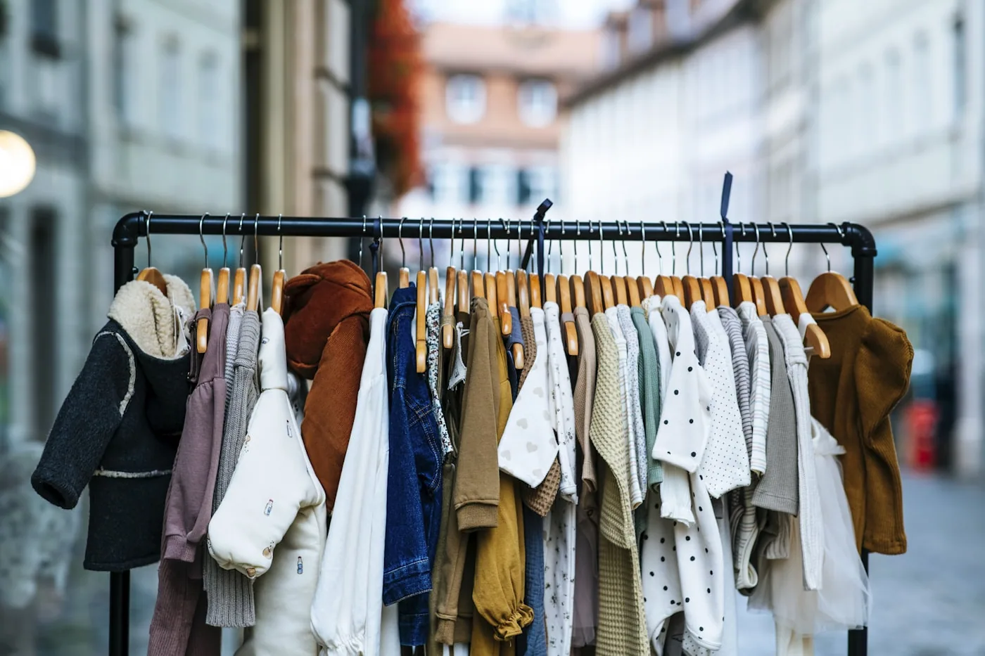 Parents comparant des vêtements pour enfants sur un portant dans une boutique, avec étiquettes et tailles visibles.