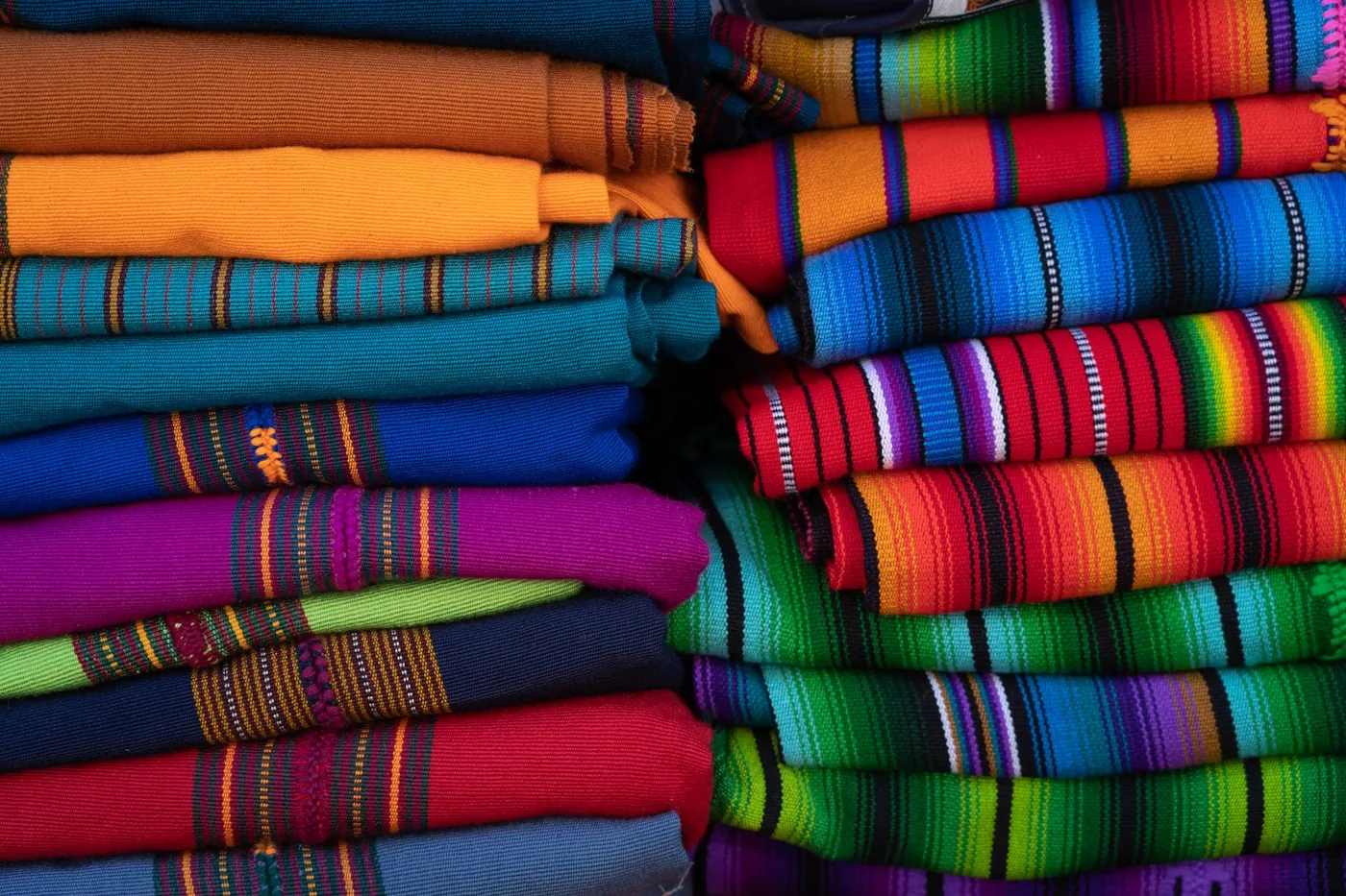 Allée d’un grand marché textile en Chine avec des stands de tissus et des rouleaux empilés.