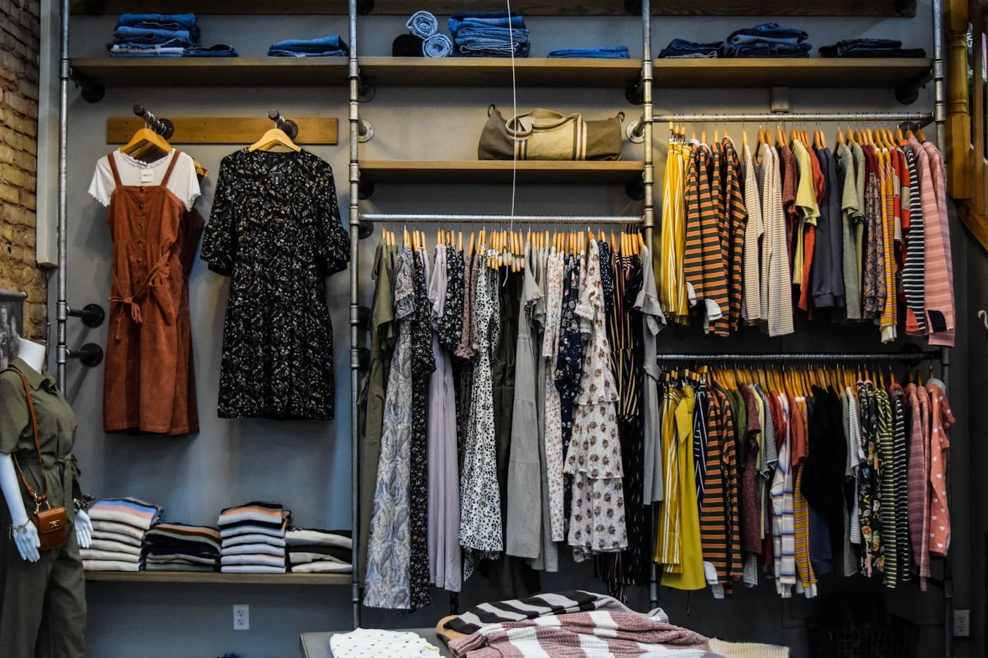 Portant de vêtements dans une boutique, avec vestes et robes classées par styles et couleurs.