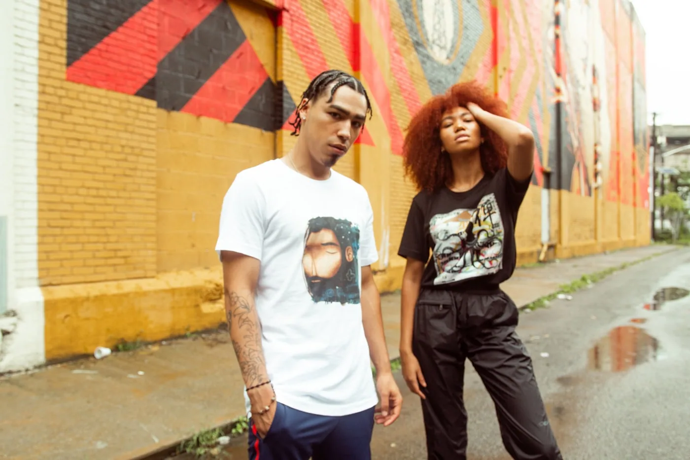 Deux silhouettes streetwear en ville, superpositions loose et logos discrets en mouvement.